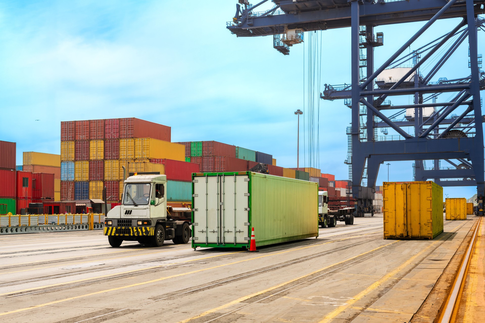 A massive container crane at the Port of San Antonio, Chile, lifts and moves the colorful stacked containers as trucks line up for transport.